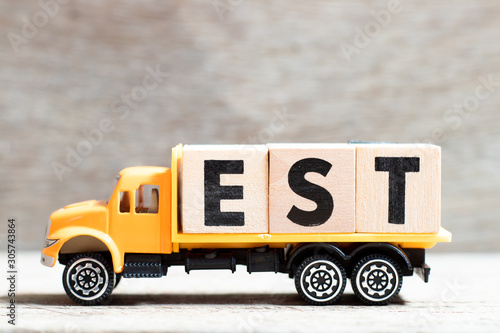 Truck hold letter block in word est (abbreviation of established, estimated, eastern time zone, expressed sequence tag) on wood background