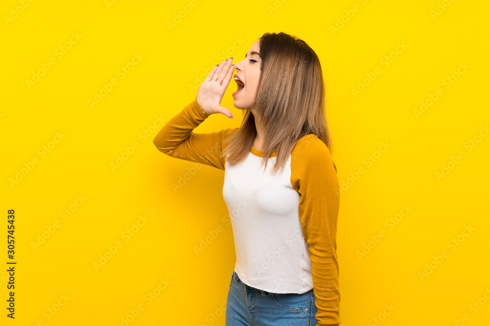 Pretty young woman over isolated yellow wall shouting with mouth wide open to the lateral Pretty young woman over isolated yellow wall shouting with mouth wide open to the lateral