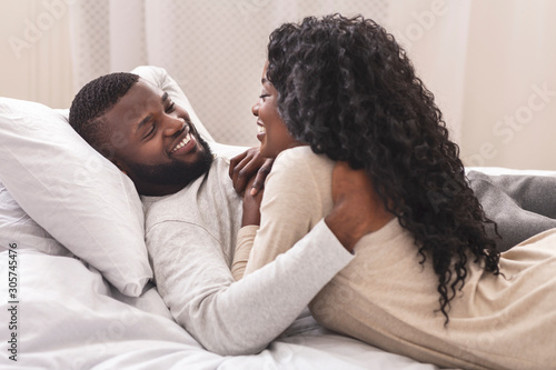 Smiling black couple having fun in bed, embracing and flirting