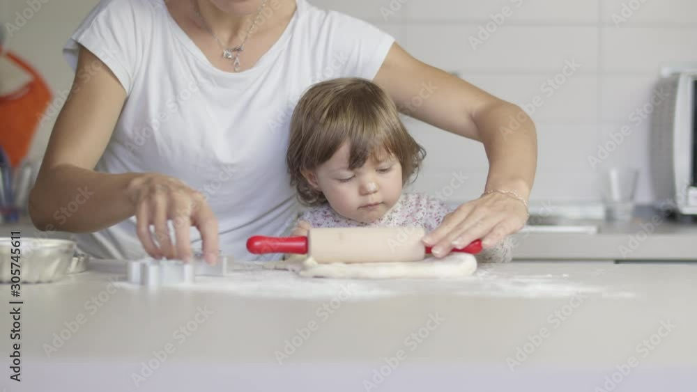 Young mother and little cute daughter cooking together preparing cookies and pizza with rolling pin and a dough in the kitchen. Playing together, having fun. Shot in 6k, cine lens. Young mother and little cute daughter cooking together preparing cookies and pizza with rolling pin and a dough in the kitchen. Playing together, having fun. Shot in 6k, cine lens.