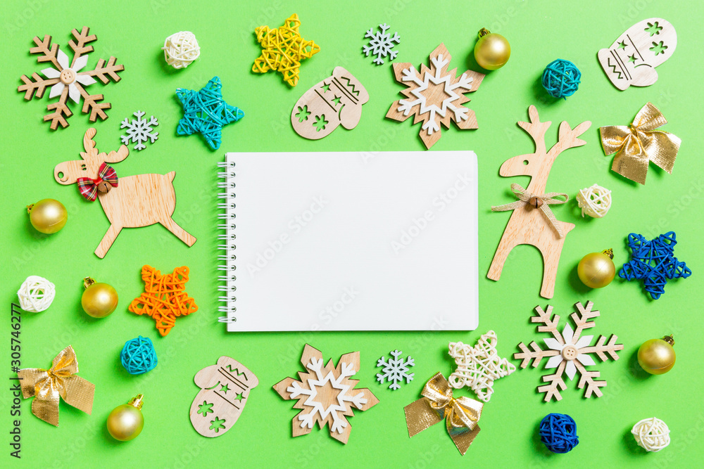 Fototapeta premium Top view of notebook on green background with New Year toys and decorations. Christmas time concept