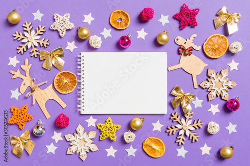 Top view of notebook surrounded with New Year toys and decorations on purple background. Christmas time concept