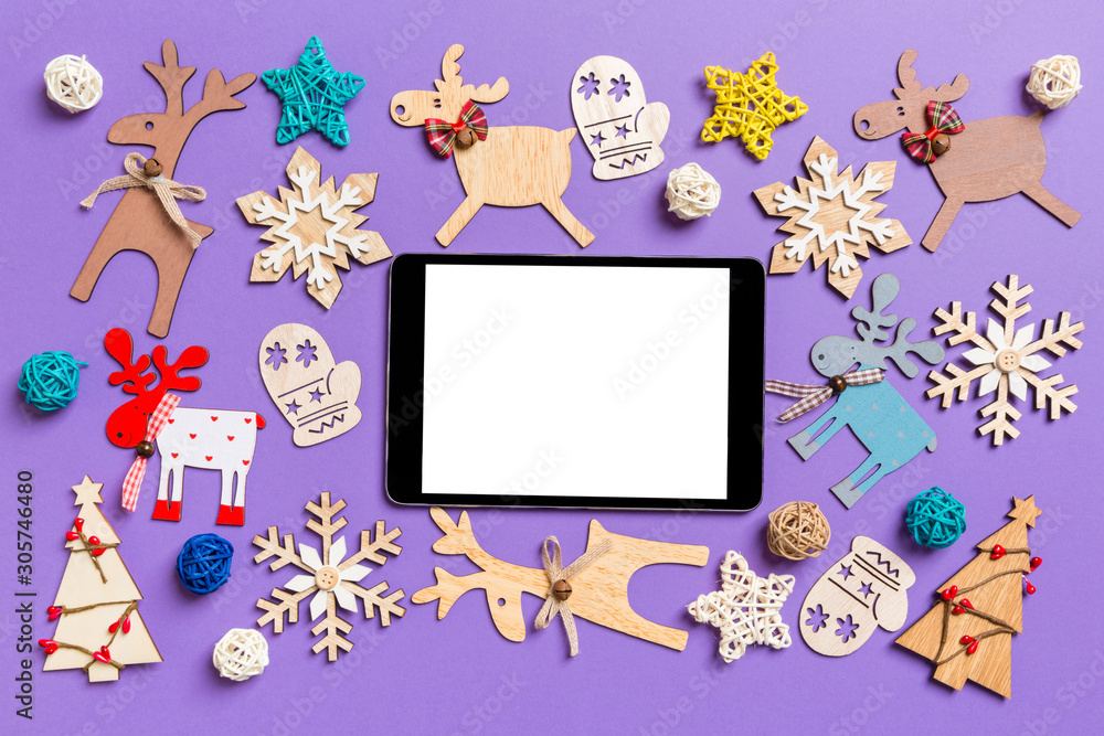 Fototapeta premium Festive decorations and toys on purple background. Top view of digital tablet. Merry Christmas concept