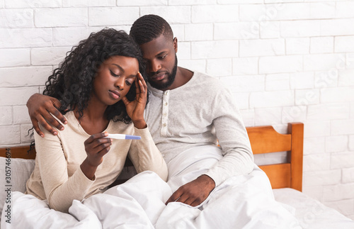Black couple sitting on bed with negative pregnancy test result photo