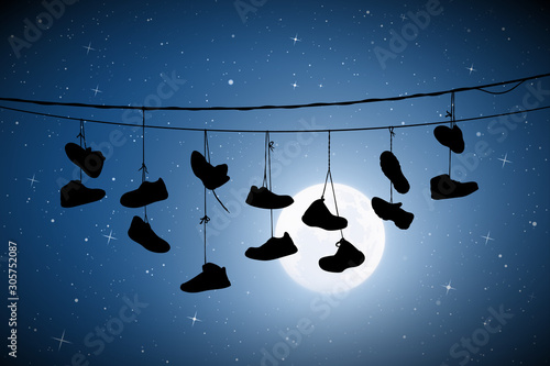 Shoes on wires on moonlit night. Vector illustration with silhouette of old shoes hanging on power lines. Full moon in starry sky