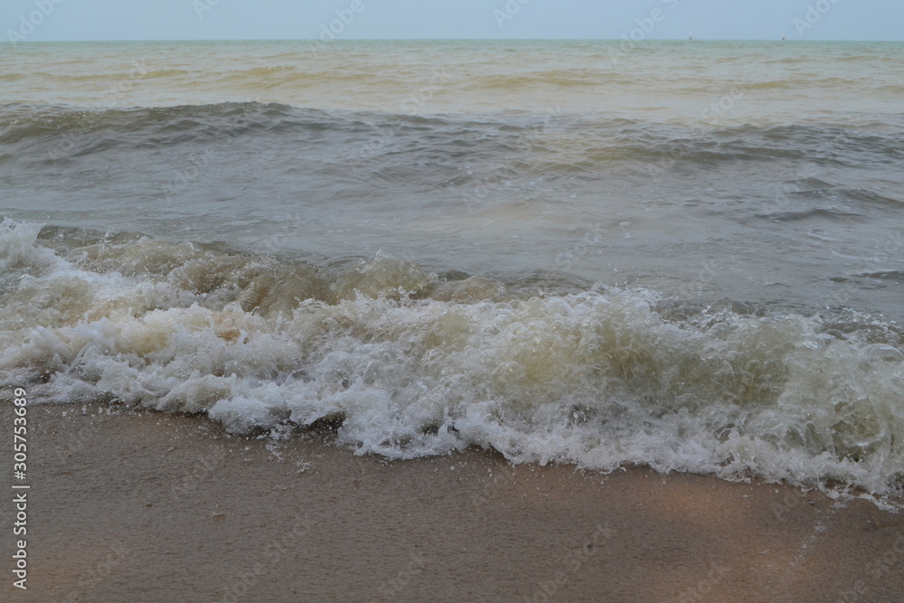 Brown-ish sea waves beside seashore, sand captured in daytime.
