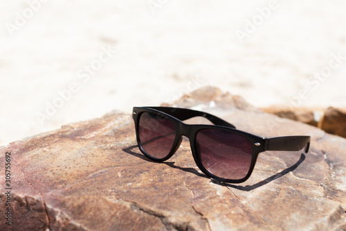 In Summer vacation. The black glasses lying on stone on sea beach.