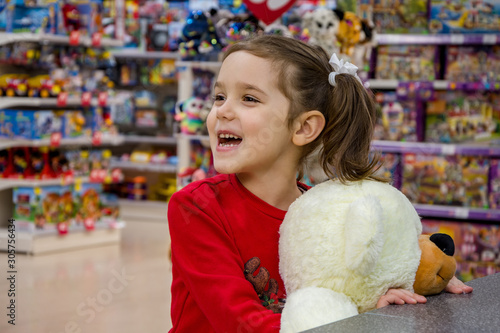 The girl calls her parents, holding a large polar bear and stands in the store among children's toys. Children's emotions, waiting for gifts and purchases.