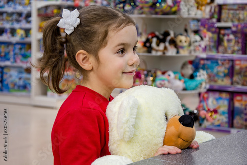 The girl smiles, holding a large polar bear and stands in the store among children's toys. Children's emotions, waiting for gifts and purchases.
