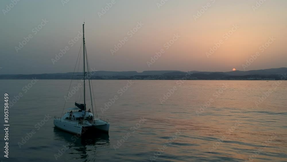 Catamaran at sunset with land insight and no wind Catamaran at sunset with land insight and no wind