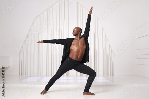 Valokuvatapetti Elegant black man dancer in black clothes is dancing in a bright room