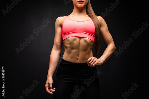 Close up of fit woman's torso with perfect abdomen muscles on black background