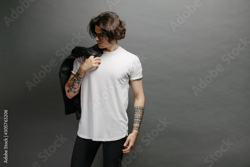 Hipster handsome male model with glasses wearing white blank t-shirt and black jeans with space for your logo or design in casual urban style photo