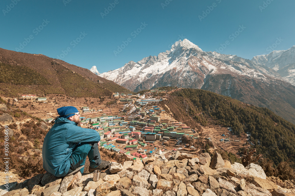 Everest trekking. Altitude and mountain sickness. A man is sitting on a hill. He has a headache. Nepal. Namche Bazaar.