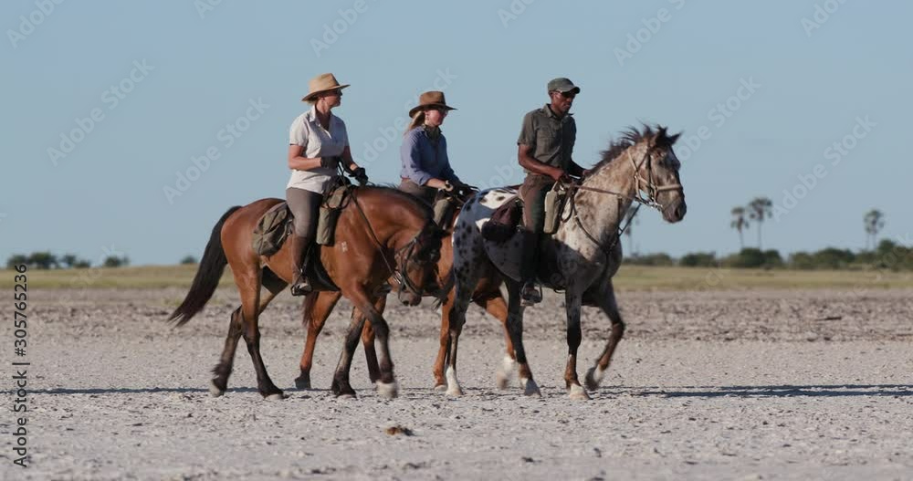 Three horse riders out on safari walking their horses across the wide open spaces of the Makgadikgadi salt Pans with blue skies in the background Three horse riders out on safari walking their horses across the wide open spaces of the Makgadikgadi salt Pans with blue skies in the background