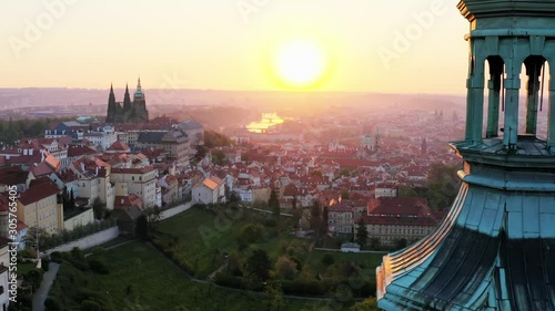 Aerial view cropped steeple of Strahov monastery at sunrise. Sun shining through belfry camera moving near towers of ancient cathedral , showing picturesque panorama above history centre of Prague 