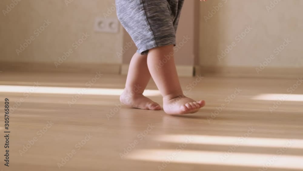 Little feet walking on floor, close-up. Baby learning to walk at home. Baby first steps. Slow motion Little feet walking on floor, close-up. Baby learning to walk at home. Baby first steps. Slow motion