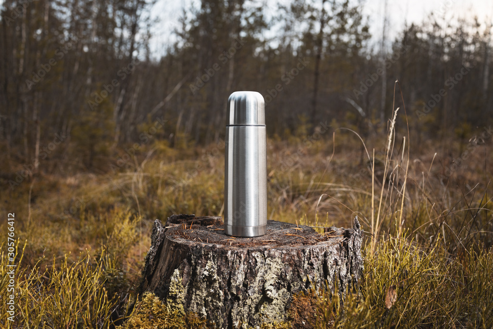 Obraz premium Stainless steel thermos with hot tea stands on a stump in the forest