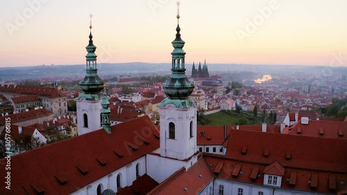 Wallpaper Mural Aerial view over Strahov monastery at sunrise. Lateral shot, drone flying opposite belfries of cathedral decorated crucifix on spire, showing picturesque panorama above Prague in early morning Torontodigital.ca