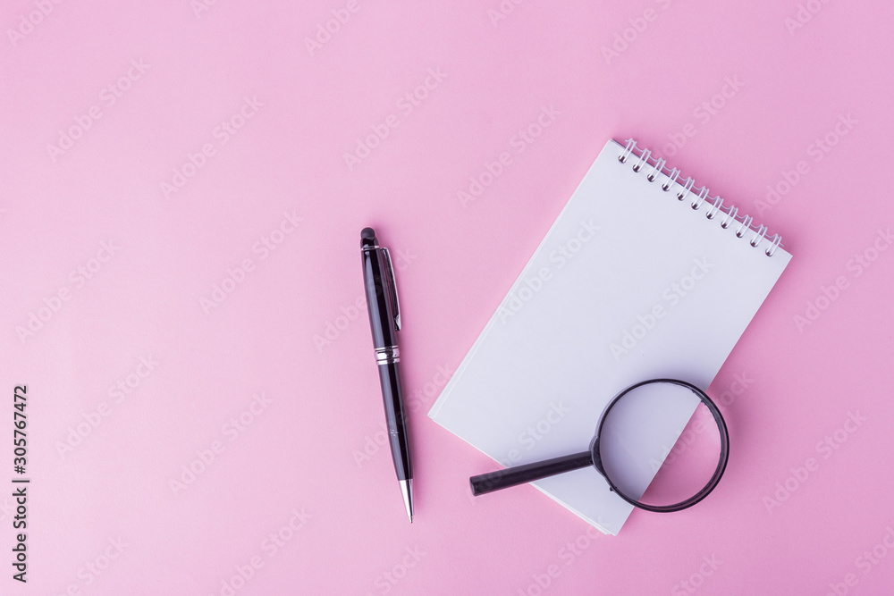 Flaylat workspace concept. An open notepad, pen and magnifying glass on pink background with copy space. Sweet soft colored tone. Flaylat workspace concept. An open notepad, pen and magnifying glass on pink background with copy space. Sweet soft colored tone.