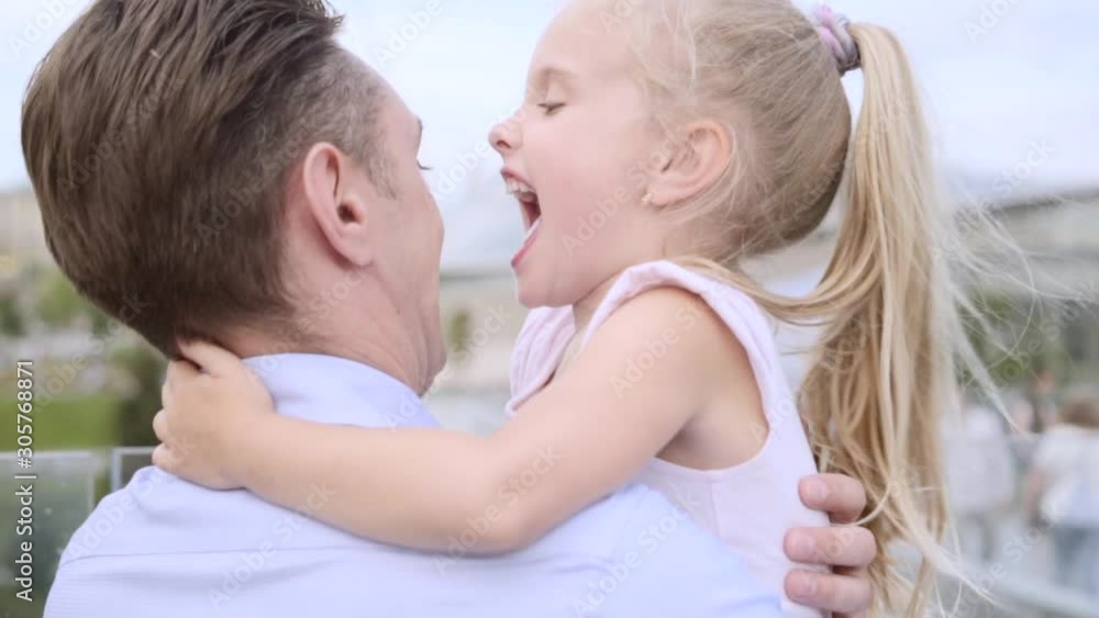 Middle-aged father embraces his daughter. Fair-haired little girl smiles happily, close up portrait, slow motion Middle-aged father embraces his daughter. Fair-haired little girl smiles happily, close up portrait, slow motion