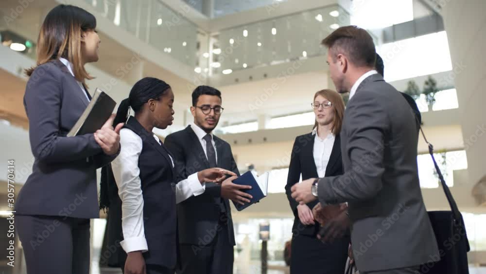 Group of six businesspeople of different ethnicities standing in the middle of business hall and discussing project before meeting Group of six businesspeople of different ethnicities standing in the middle of business hall and discussing project before meeting
