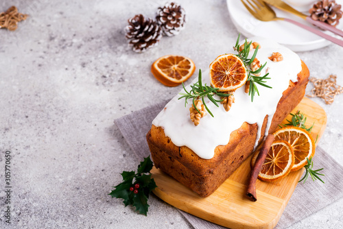Fruit loaf cake dusted with icing, nuts and dry orange on stone background. Christmas and Winter Holidays