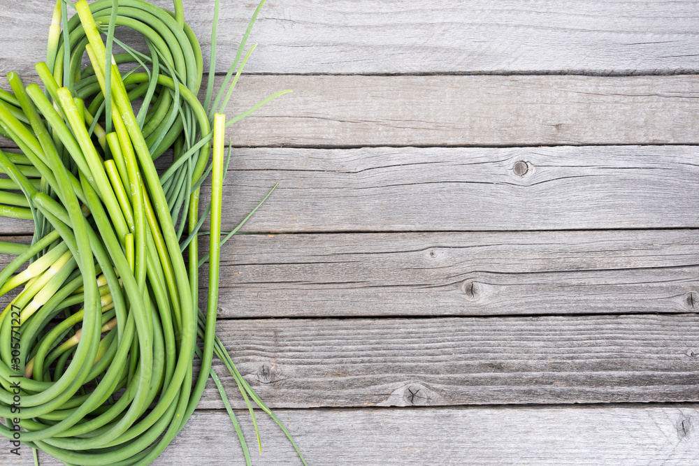 Green stalks of garlic on wooden table. The twisted stems of plants from seed. Preparation of summer salad for healthy diet Green stalks of garlic on wooden table. The twisted stems of plants from seed. Preparation of summer salad for healthy diet