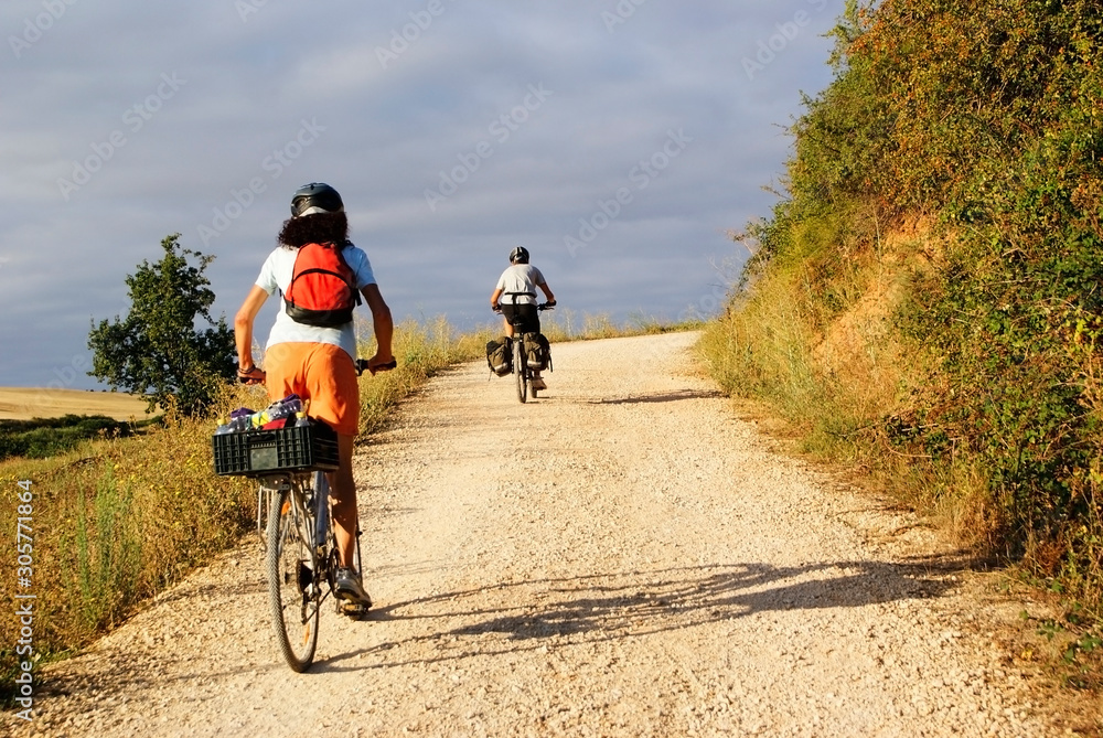 Couple of travelers on a touring bike traveling on a rural road in Spain in the direction of Santiago de Compostela.