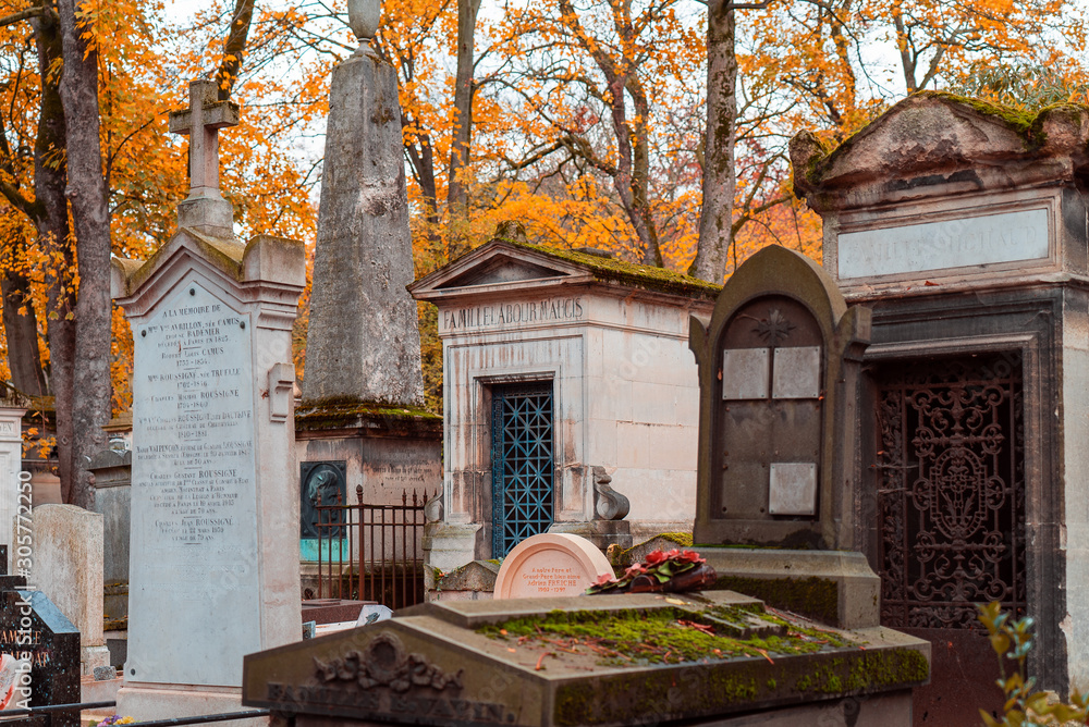 A view on autumn alley of the most famous cemetery of Paris Pere Lachaise, France. Tombs of various famous people. Golden autumn over eldest tombs.