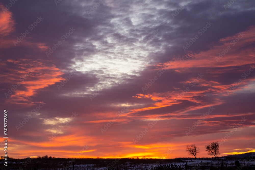 Red-blue sunset with dark clouds on the outskirts of the village. Dark winter rural silhouette with a beautiful sunrise. Artistically blurry