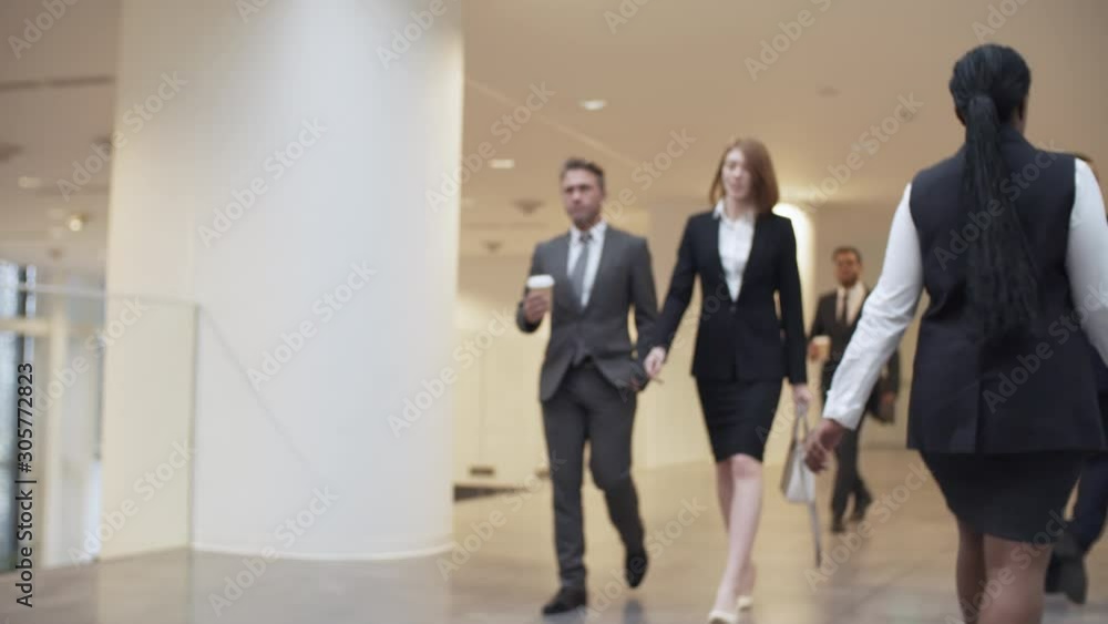 Group of two businesspeople, man and woman, walking to work through office building and talking to each other, man holding cup of takeaway coffee Group of two businesspeople, man and woman, walking to work through office building and talking to each other, man holding cup of takeaway coffee