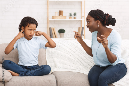 Afro woman lecturing her child who closing ears