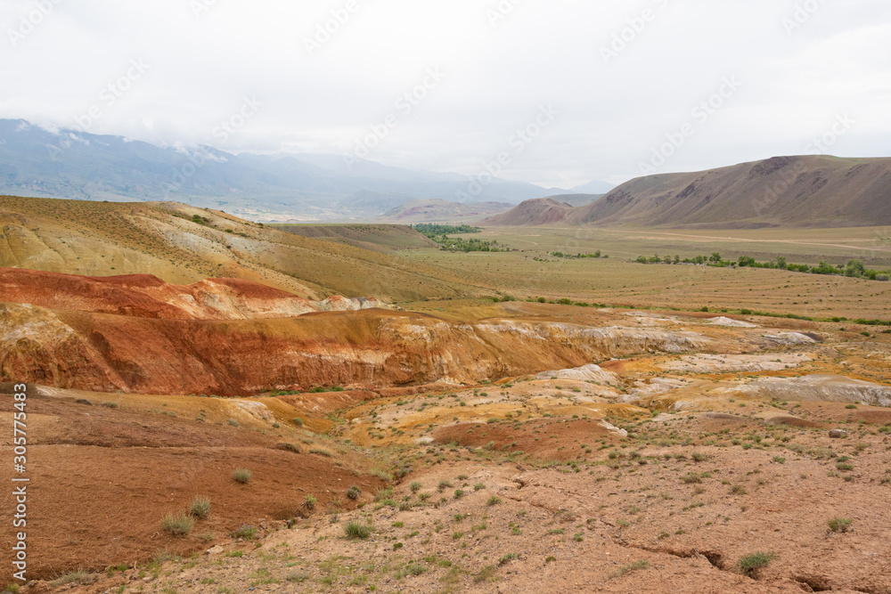 Colored hills in mountain valley. Dry sandy red hills on hot summer day. Drought, climate change. Soil erosion in ravines