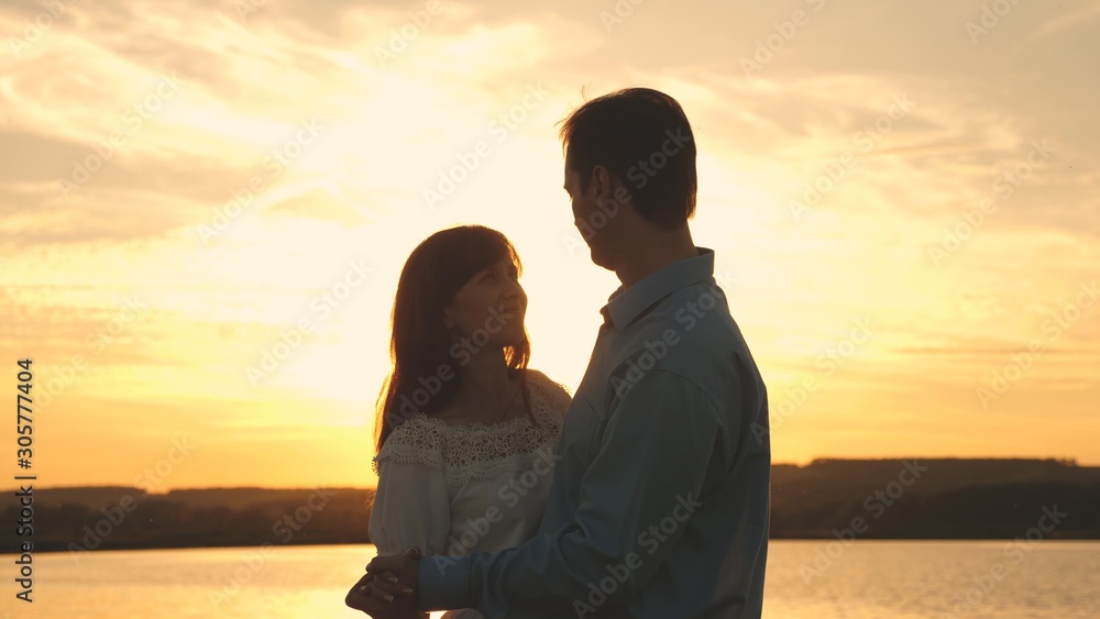 Young couple dancing at sunset on beach. Loving man and woman dance in bright rays of sun on background of the lake. Happy guy and girl waltz in the evening in the summer park.