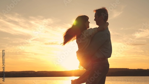 Happy guy and girl waltz in evening in the summer park. Loving man and woman dance in bright rays of sun on the background of the lake. Young couple dancing at sunset on beach.