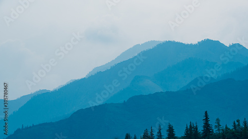 silhouettes of mountains in blue haze. Outline of gentle hills in the valley © Koirill