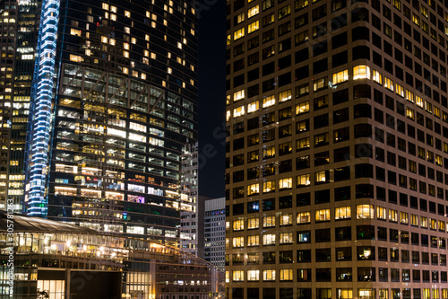 Modern skyscrapers at night with colorful glowing windows, lights, and reflections depicting concepts of business, economy, employment, work, commerce