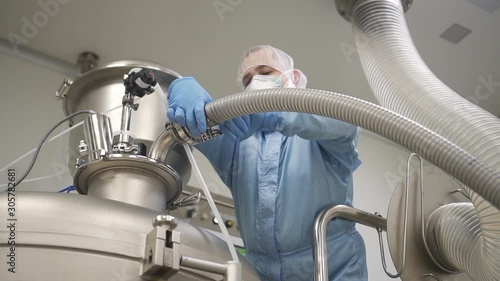 male worker is adjusting metal machine pipe in a workshop of pharmaceutical factory. engineer operating machinery on plant. mixing powder and granules. man turning control process