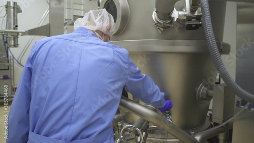 Worker control the containers pharmaceutical producrion manufacturing equipment. lab drug factory worker checking and adjusting production steel machines and containers photo