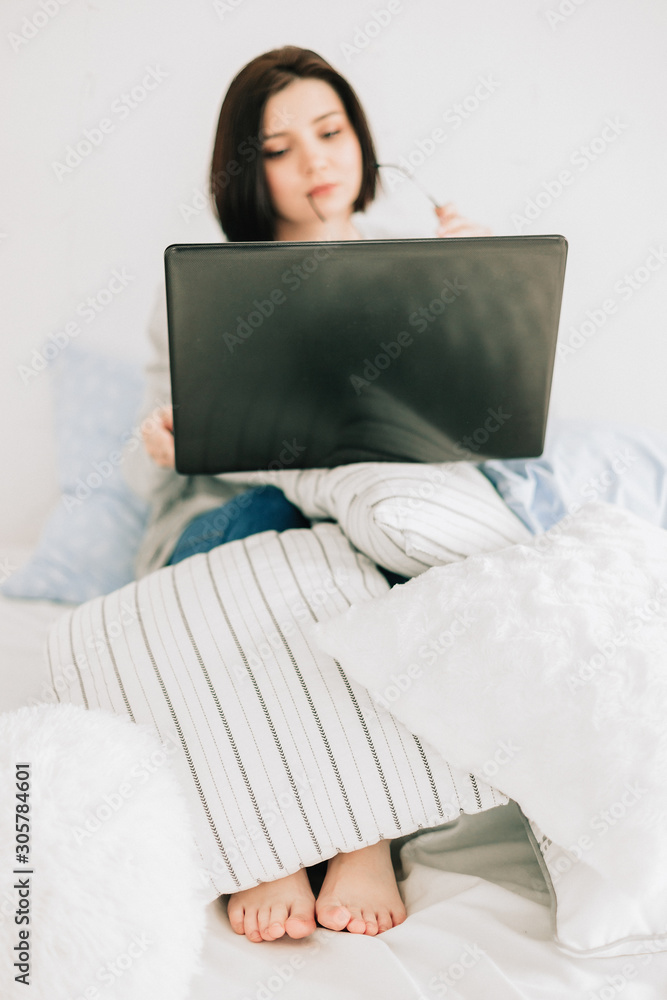 Businesswoman working on her laptop in the white bed. Work at home. Freelancer lifestyle Businesswoman working on her laptop in the white bed. Work at home. Freelancer lifestyle