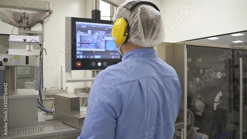 Worker control process of sorting pills into packages. Pharmacist control pharmaceutical manufacturing process at drug factory using touchscreen computer. protective suit and setting concept