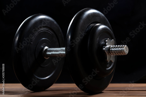 Big black male dumbbell on a brown wooden table on a black background