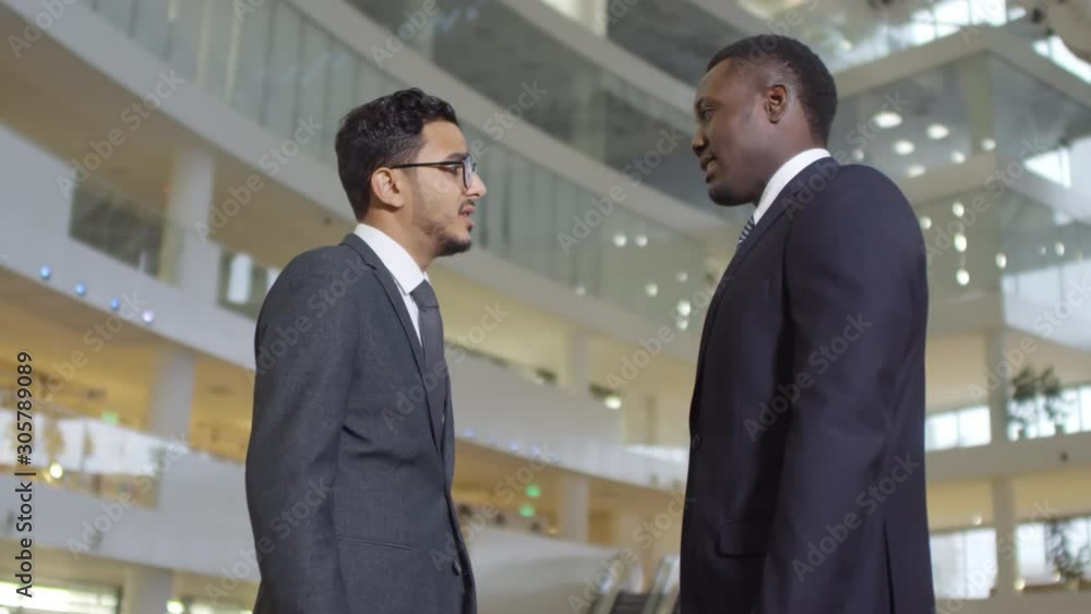 Side view medium shot of two multiethnic businessmen shaking hands with each other and walking away Side view medium shot of two multiethnic businessmen shaking hands with each other and walking away