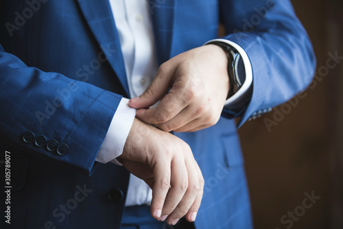 A man in an elegant suit adjusts his shirt sleeve.