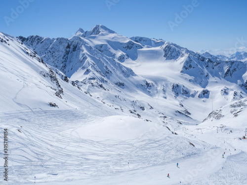 Winter landscape with snow covered mountain slopes and pistes with skiers enjoying spring sunny day at ski resort Stubai Gletscher, Stubaital, Tyrol, Austrian Alps