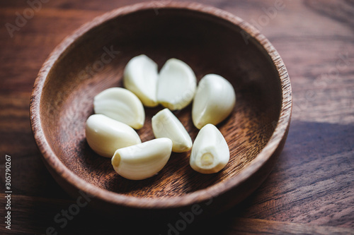 Macro food photography of peeled garlic cloves in a wooden bowl. Top view.