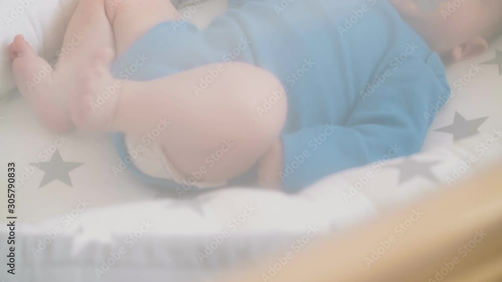 lovely newborn child in blue bodysuit kicks bare legs sucking pacifier in nice cocoon in cot behind chiffon closeup lovely newborn child in blue bodysuit kicks bare legs sucking pacifier in nice cocoon in cot behind chiffon closeup