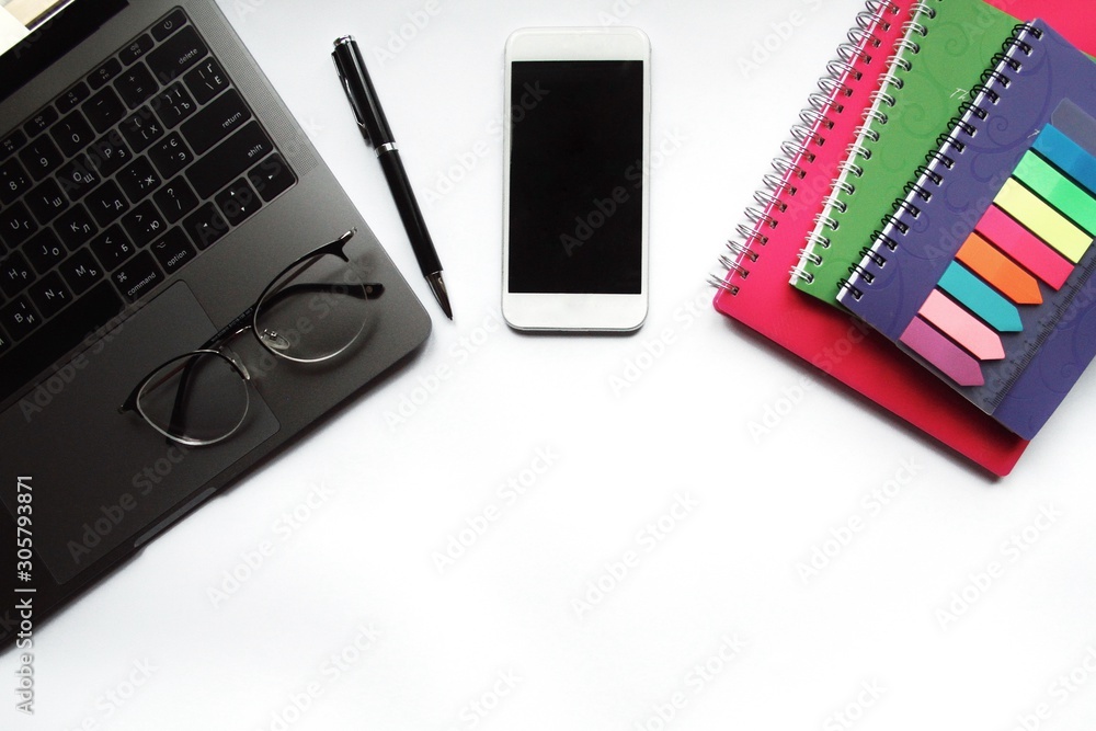 Desk with laptop, eye glasses, pen and smartphone screen. Top view with copy space.