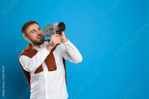 Young man with vintage video camera on light blue background, space for text